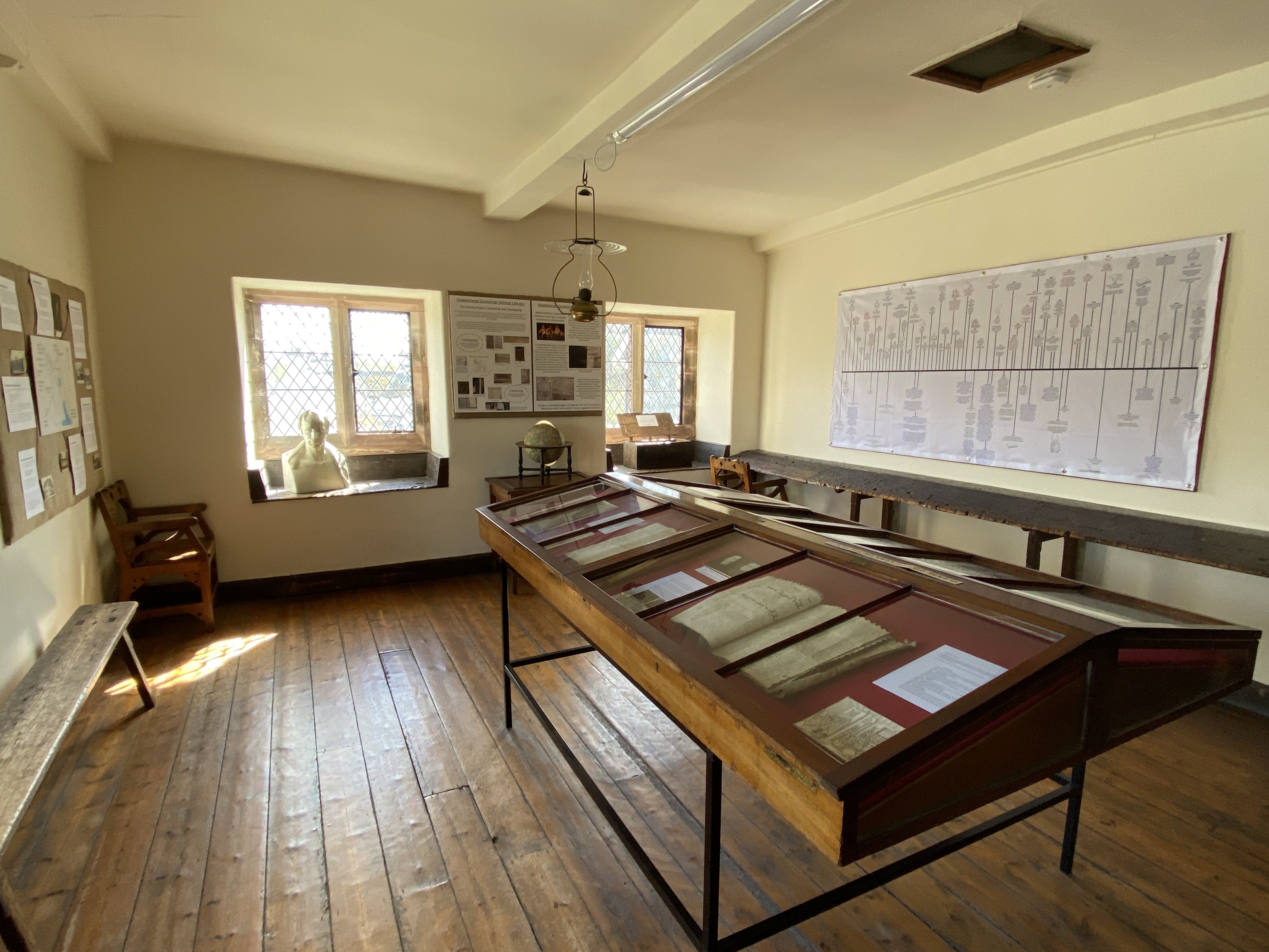 Photograph of exhibition room showing a table cabinet in the centre of the room which contains old documents and information panels, on the wall of the room is a timeline. 