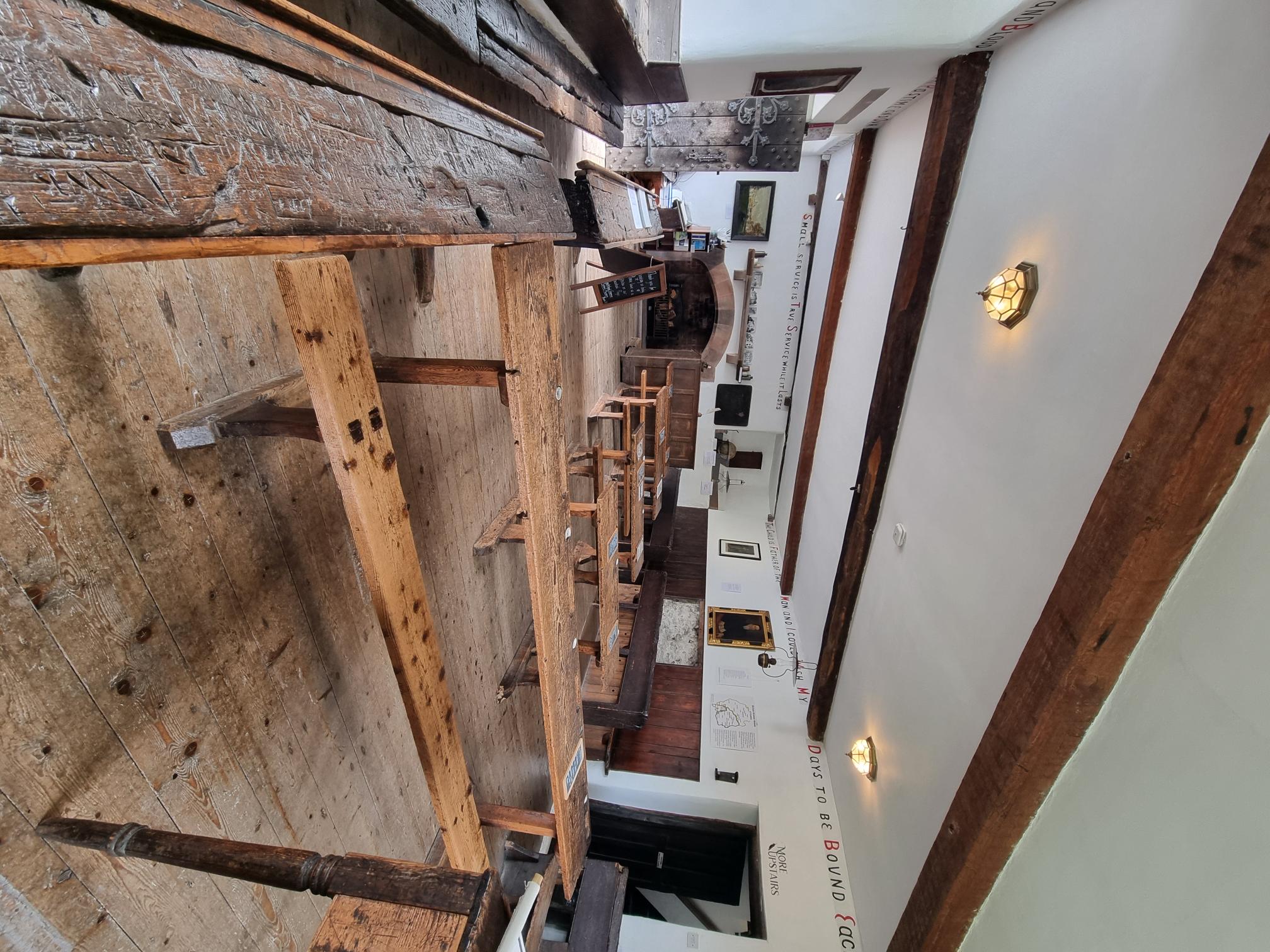 Classroom with historic wooden desks at the sides and in rows through the middle. The room has white walls and wooden beams. 